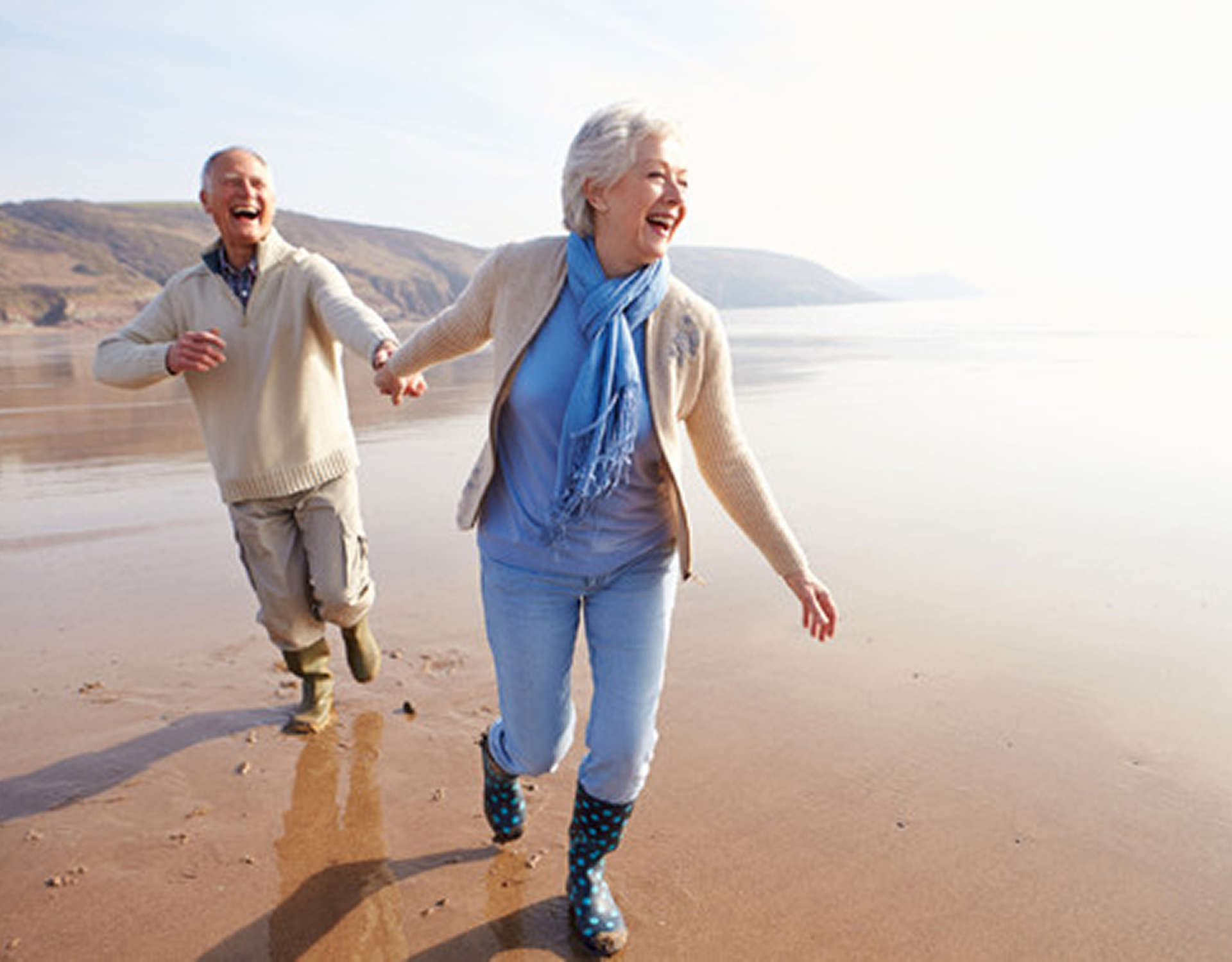 Elderly couple joyfully walking on the beach.