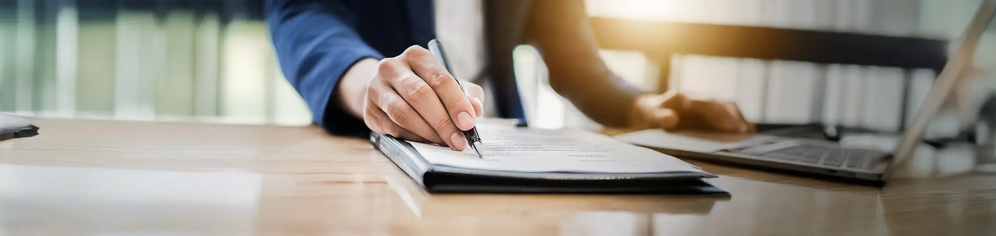 Person signing document at a desk.
